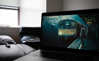 A laptop displaying an artistic image of a submerged train station, set in a dim room with a couch in the background.