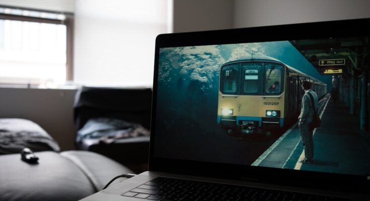 A laptop displaying an artistic image of a submerged train station, set in a dim room with a couch in the background.