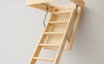 A wooden loft ladder partially extended from a ceiling opening against a plain wall